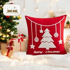 a red christmas pillow sitting on top of a white blanket next to a christmas tree