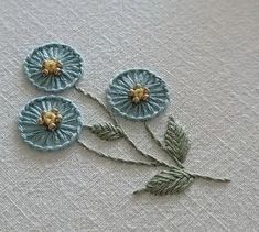 three blue flowers with green leaves on a white table cloth, one is embroidered onto the fabric