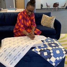 a woman sitting on a blue couch working on some quilting material in an office