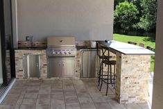 an outdoor kitchen with stainless steel appliances and bar stools next to the bbq