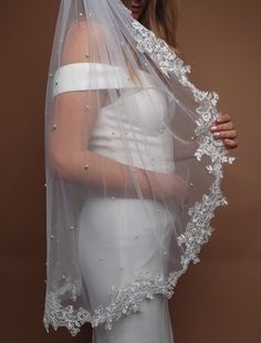 a woman wearing a wedding veil with flowers on the side and beading around the edge