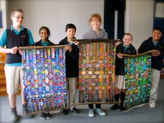 several children holding up art pieces made out of paper and cardboard with the teacher standing behind them