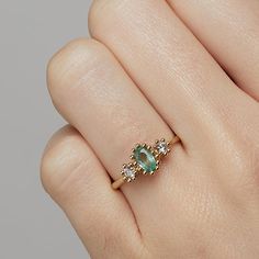 a woman's hand holding a ring with an emerald and white diamond in it