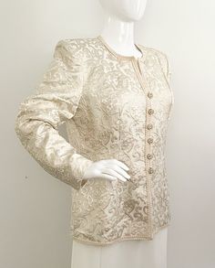 This is a stunning ivory and gold jacket from Lillie Rubin.  It is fully lined and has shoulder pads.  Closes down the front with rhinestone buttons and inner snaps.  The jacket has beautiful ivory trim.  The metallic gold thread and the textured pattern really add to the elegance of this piece.  Size tag 10, made in USA.   Measurements taken with jacket laying flat and doubled where appropriate. In order to determine fit we recommend comparing measurements with an item that fits you well. Lengt Glamorous Spring Wedding Blazer, Elegant White Embellished Blazer, Fall Wedding Silk Outerwear, Fitted Silk Outerwear For Wedding, Gold Blazer With Gold Buttons For Spring, Elegant Fitted Blazer With Gold Buttons, Elegant Formal Outerwear With Gold Buttons, Elegant Evening Blazer With Gold Buttons, Evening Blazer With Gold Buttons And Long Sleeves