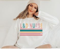 a woman sitting on a bed wearing a white sweatshirt with the word love and nurse printed on it