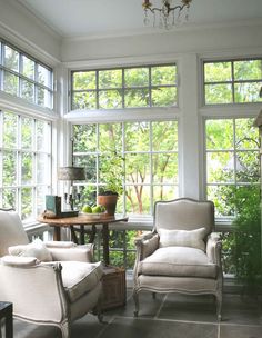 two chairs and a table in front of large windows with potted plants on them