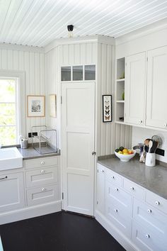 a kitchen with white cabinets and gray counter tops, along with a bowl of fruit on the counter