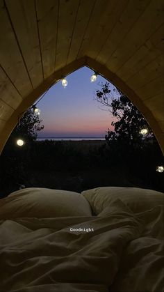 a bed with white sheets and pillows under a wooden arch over looking the ocean at night