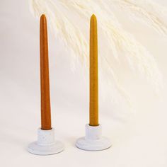 two white and brown candles are next to each other with feathers in the back ground