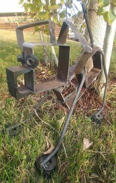 a metal sculpture sitting in the grass next to a tree