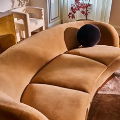 a brown couch sitting in front of a window next to a table with a vase on it