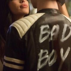 a young man and woman standing next to each other wearing leather jackets with writing on them