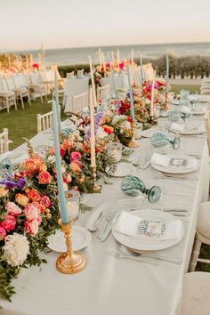 a long table is set up with flowers and candles for an outdoor wedding reception at the beach