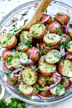 a glass bowl filled with red potatoes and onions, garnished with parsley