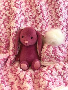 a pink and white crocheted blanket with a stuffed animal in it's lap