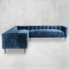 a blue velvet sectional sofa sitting on top of a white floor next to a gray wall