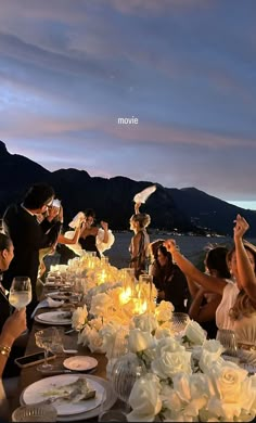 a group of people sitting around a table with food and wine glasses on top of it