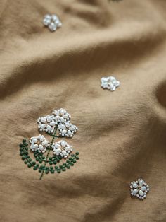 an embroidered fabric with white flowers and green leaves on it's side, as well as beads in the center