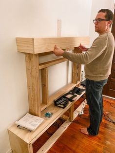 a man standing in front of a wooden shelf with electronics on it and wires coming from underneath