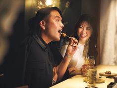 a man and woman sitting at a table with food in front of them, eating