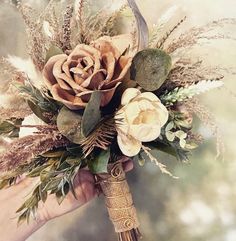 a bridal bouquet with dried flowers and foliage in someone's hand on a blurry background