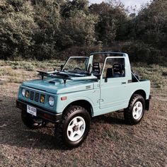 a light blue pick up truck parked on top of a grass covered field with trees in the background