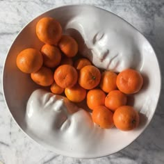 a white bowl filled with oranges next to a face on a marble counter top