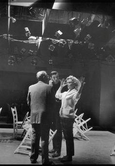 black and white photograph of three people standing in front of a stage with chairs on it