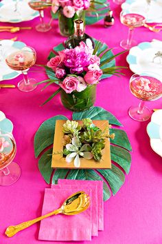 the table is set with pink and yellow plates, napkins, and gold utensils