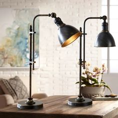 two desk lamps sitting on top of a wooden table next to a vase with flowers