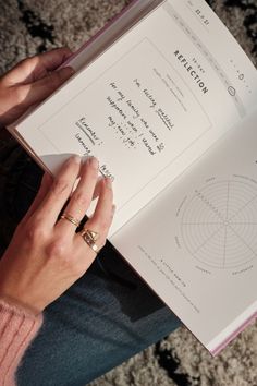 a woman is holding an open book in her hands and reading it on the floor