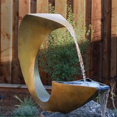 a water fountain is shown in the middle of a garden area with a wooden fence behind it