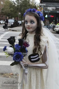 a doll dressed as a bride with makeup and flowers in her hand on the street