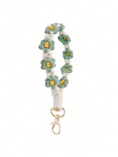 a white and green bracelet with yellow flowers on it's end, hanging from a metal hook