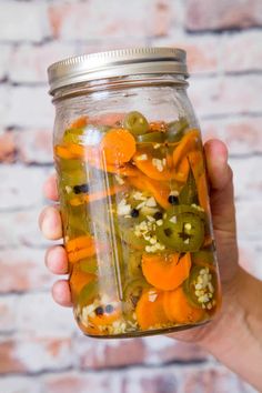 a person holding a jar full of pickles and peppers