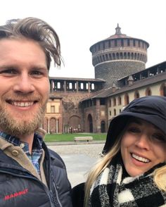 a man and woman standing next to each other in front of an old brick building