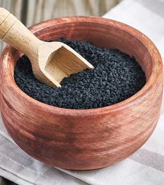 a wooden bowl filled with black sesame seeds and a wooden spoon in the top right corner