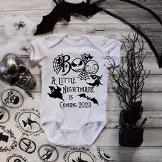 a baby bodysuit that says little night mare coming next to it is decorated with halloween decorations