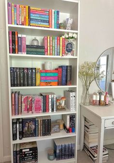 a white book shelf filled with books next to a dresser and mirror on the wall