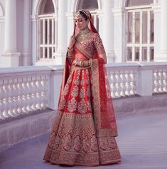 a woman in a red and gold bridal gown standing on a balcony looking at the camera