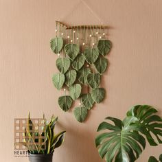 a wall hanging made out of green leaves next to a potted plant