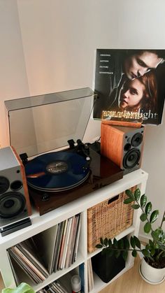 a record player sitting on top of a white shelf next to a plant and cd player