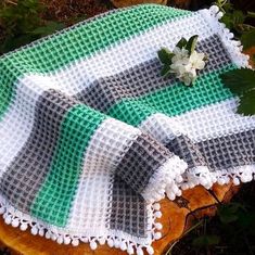 a green and white blanket sitting on top of a piece of wood next to flowers