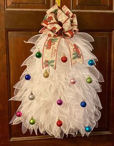 a christmas tree door hanger decorated with ornaments and ribbon hanging from the front door