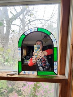 a person taking a selfie in front of a stained glass window with trees outside