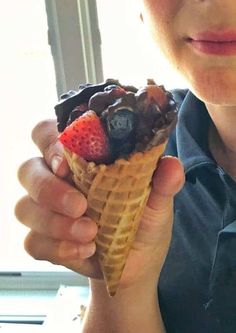 a person holding an ice cream cone filled with fruit