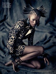 a woman sitting on the ground wearing a leopard print dress with feathers in her hair