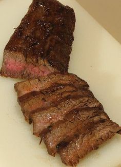 two pieces of steak sitting on top of a white cutting board next to a knife