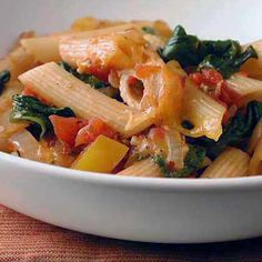 pasta with spinach and tomato sauce in a white bowl on a tablecloth cloth