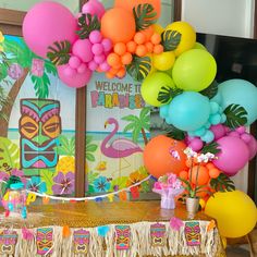 there is a table with balloons and decorations on it in front of a wall that says welcome to paradise